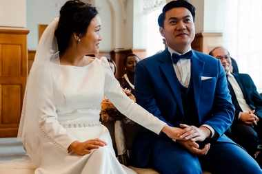 A touching and intimate moment between the bride and groom during their wedding ceremony at the gemeente Rotterdam. While the groom is visibly moved as he listens to their journey together, the bride reaches out for his hands to embrace him – captured by DiscussTomorrow Studio.