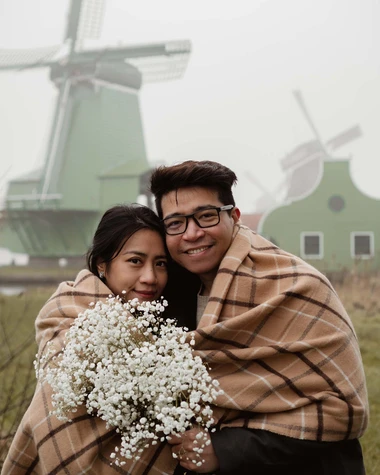 A vibrant couple looks into the camera on a cold misty day at the Zaanse Schans, Netherlands